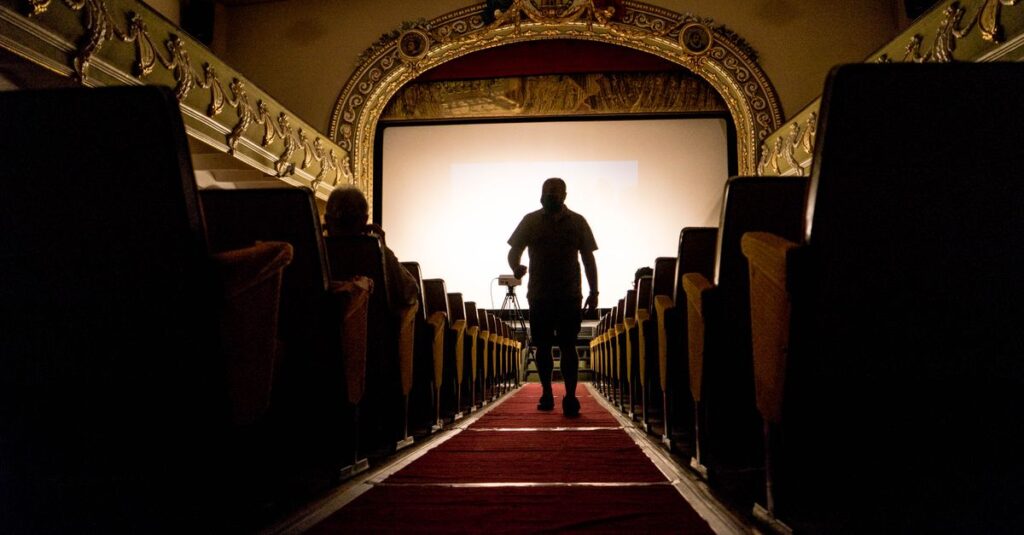 A person walking down an aisle in a vintage theater, showcasing ornate decor.